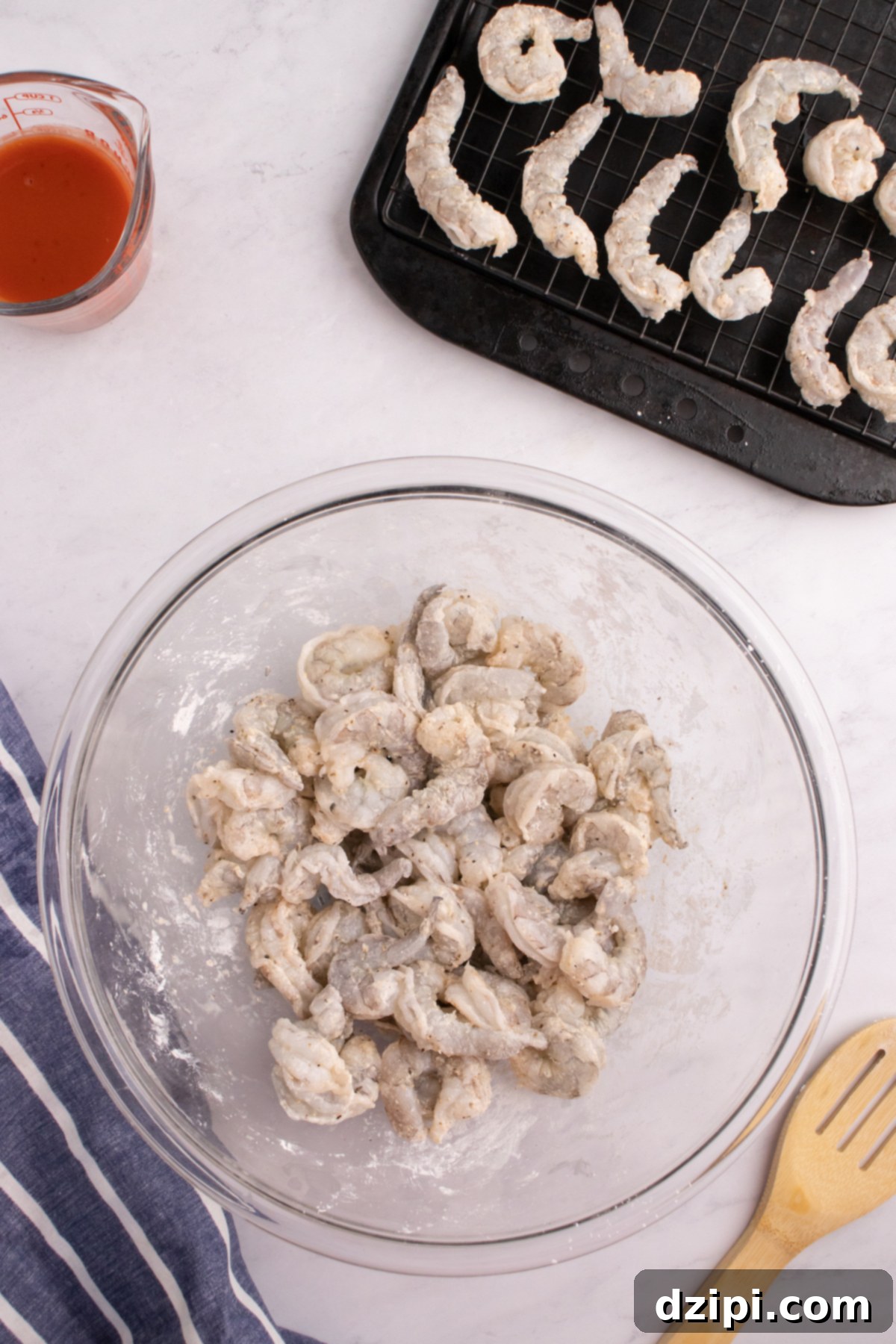 Raw shrimp tossed with cornstarch and spices in a mixing bowl.