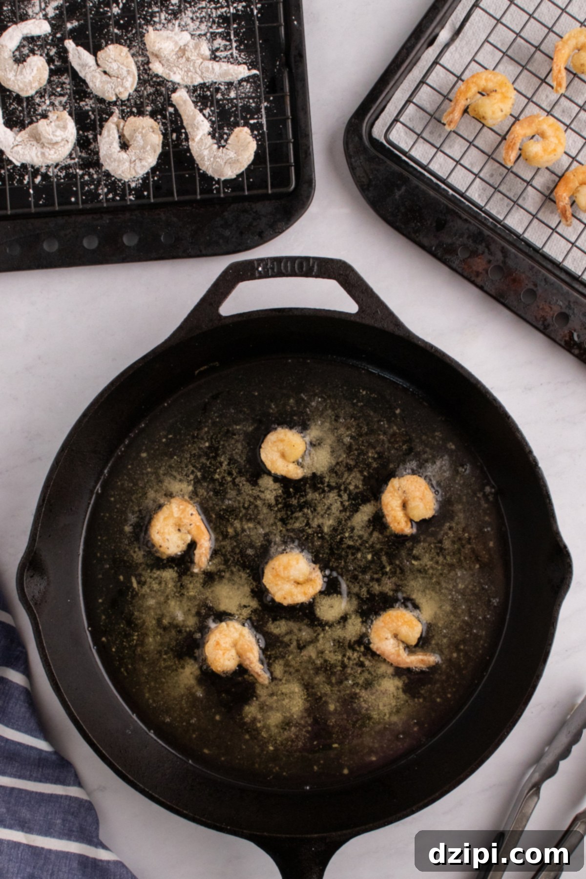 Six breaded shrimp frying in a cast iron pan filled with hot oil.