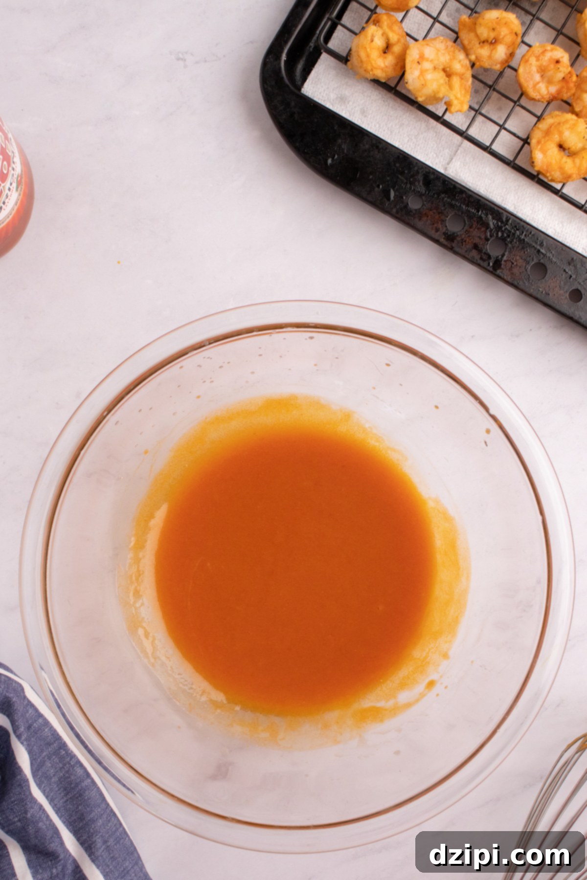 A glass mixing bowl filled with hot sauce and melted butter.