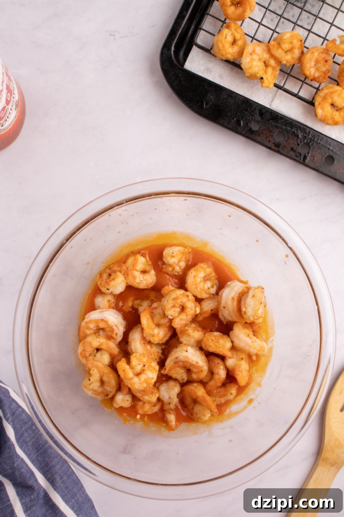 Fried shrimp being coated with buffalo sauce in a glass mixing bowl.