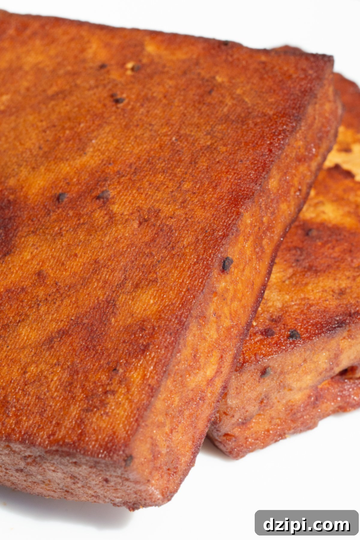 Two blocks of tofu that have turned deep red from marinating in bbq sauce and being smoked on the grill on a white serving plate.