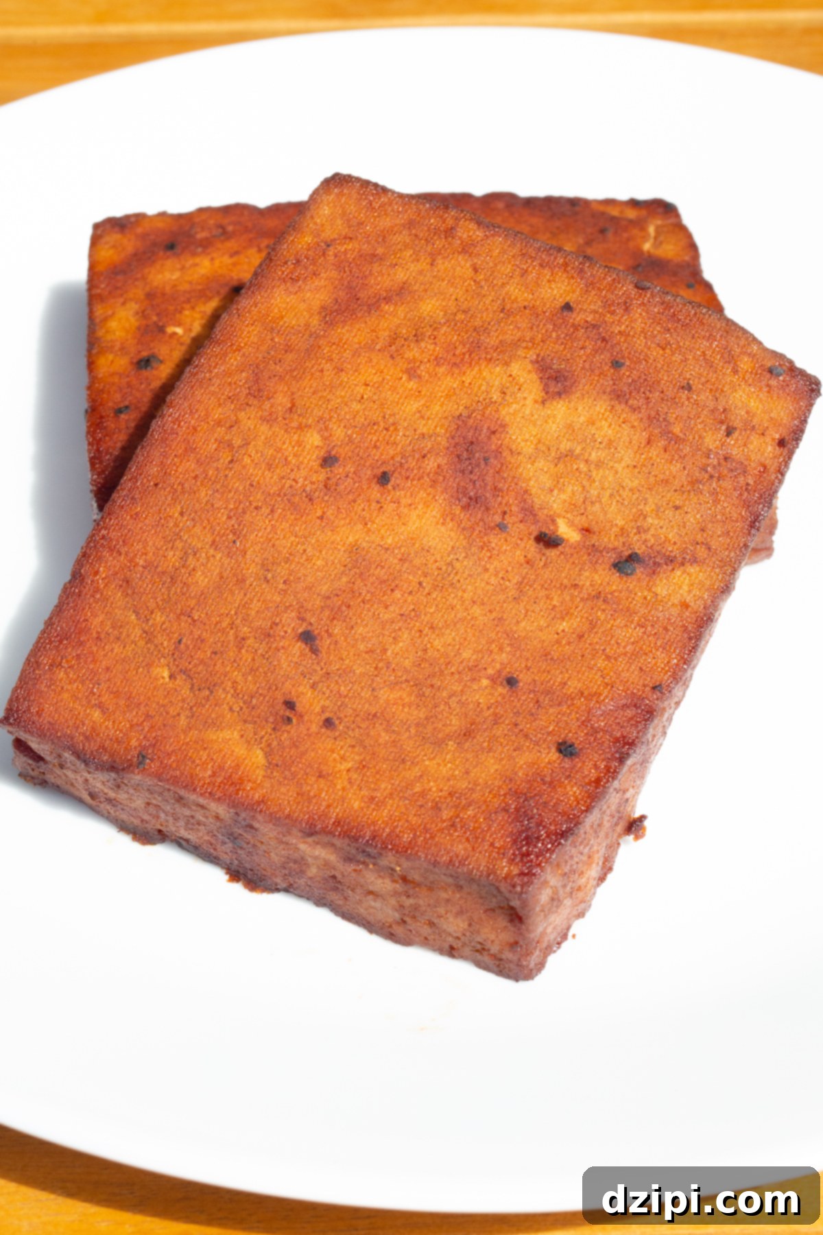 Two blocks of smoked tofu that have been turned a deep red by the barbecue sauce sit on a white serving plate.