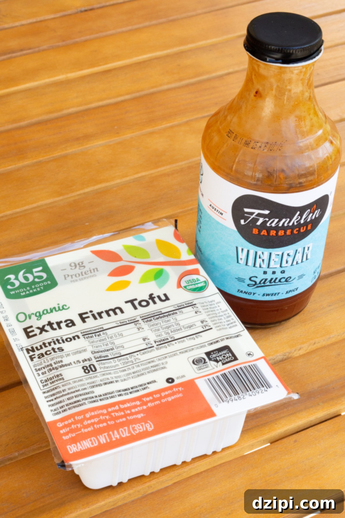 A package of extra firm tofu and a bottle of bbq sauce on a wooden outdoor table.