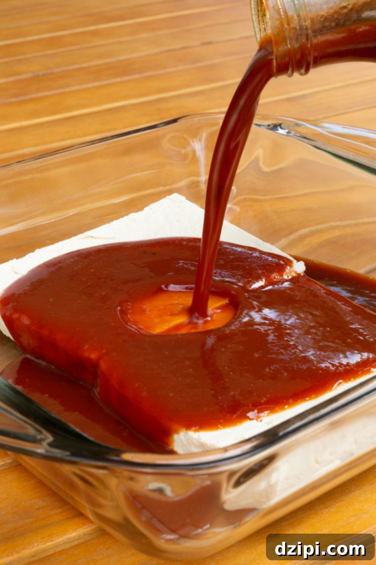 Sliced tofu halves submerged in BBQ sauce in a baking dish.