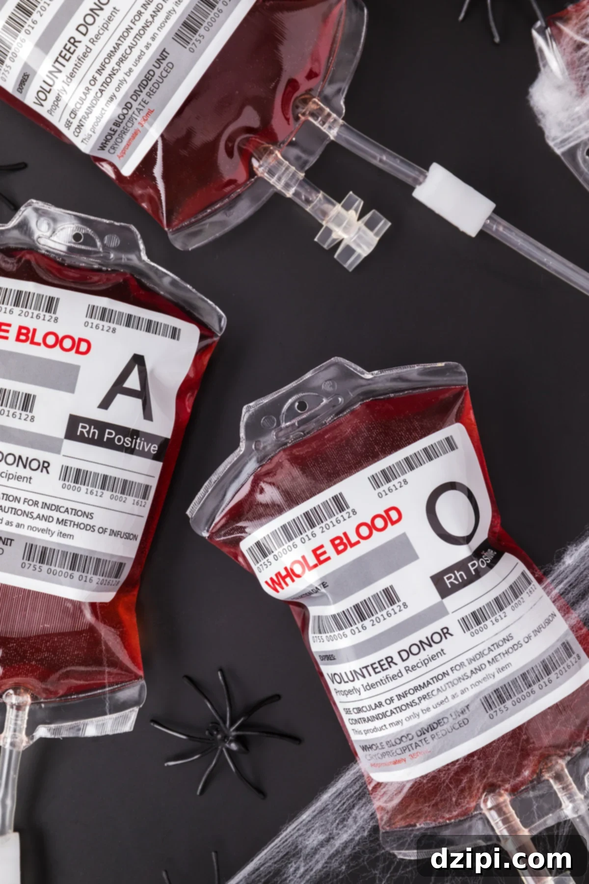 Three novelty IV bags filled with red punch on a black background. Plastic spiders and fake spider webs surround them.