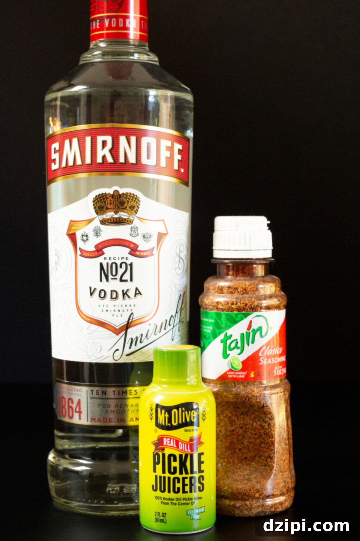 All the ingredients to make pickle shots on a black background - a bottle of vodka, Tajin, and pickle juice.