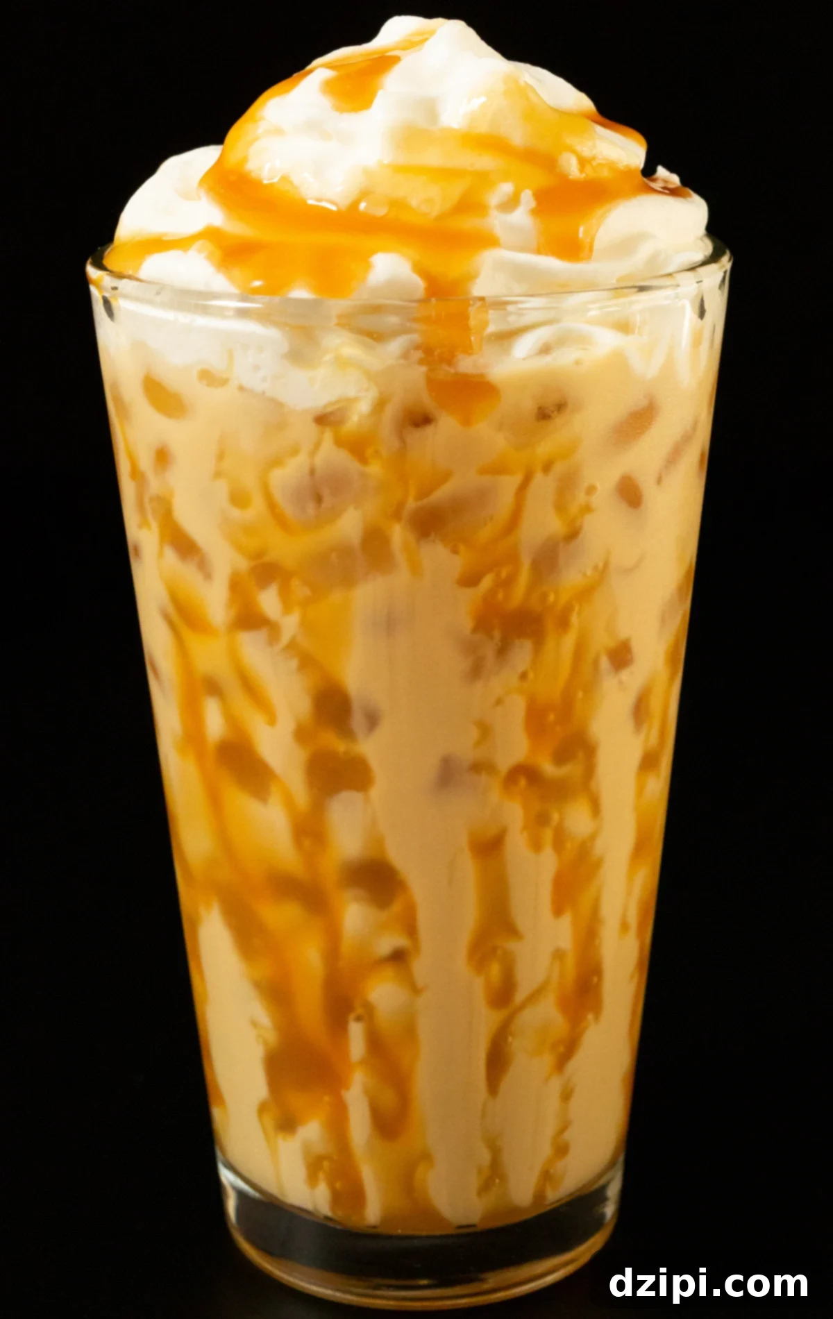 A pint glass has caramel drizzled all around the inside and is filled with a light brown butterbeer latte topped with whipped cream and caramel, evoking a Harry Potter theme.