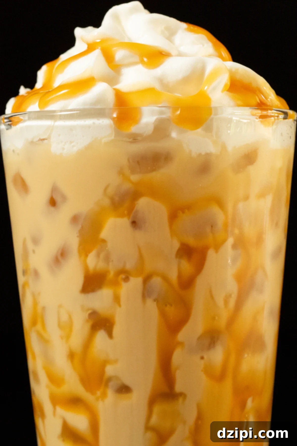 Close up of a butterbeer latte in a pint glass. Caramel has been drizzled all over the inside of the glass and on top of the whipped cream topping, highlighting its delicious appeal.