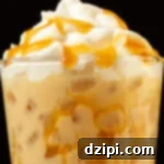 Close up of a butterbeer latte in a pint glass. Caramel has been drizzled all over the inside of the glass and on top of the whipped cream topping.