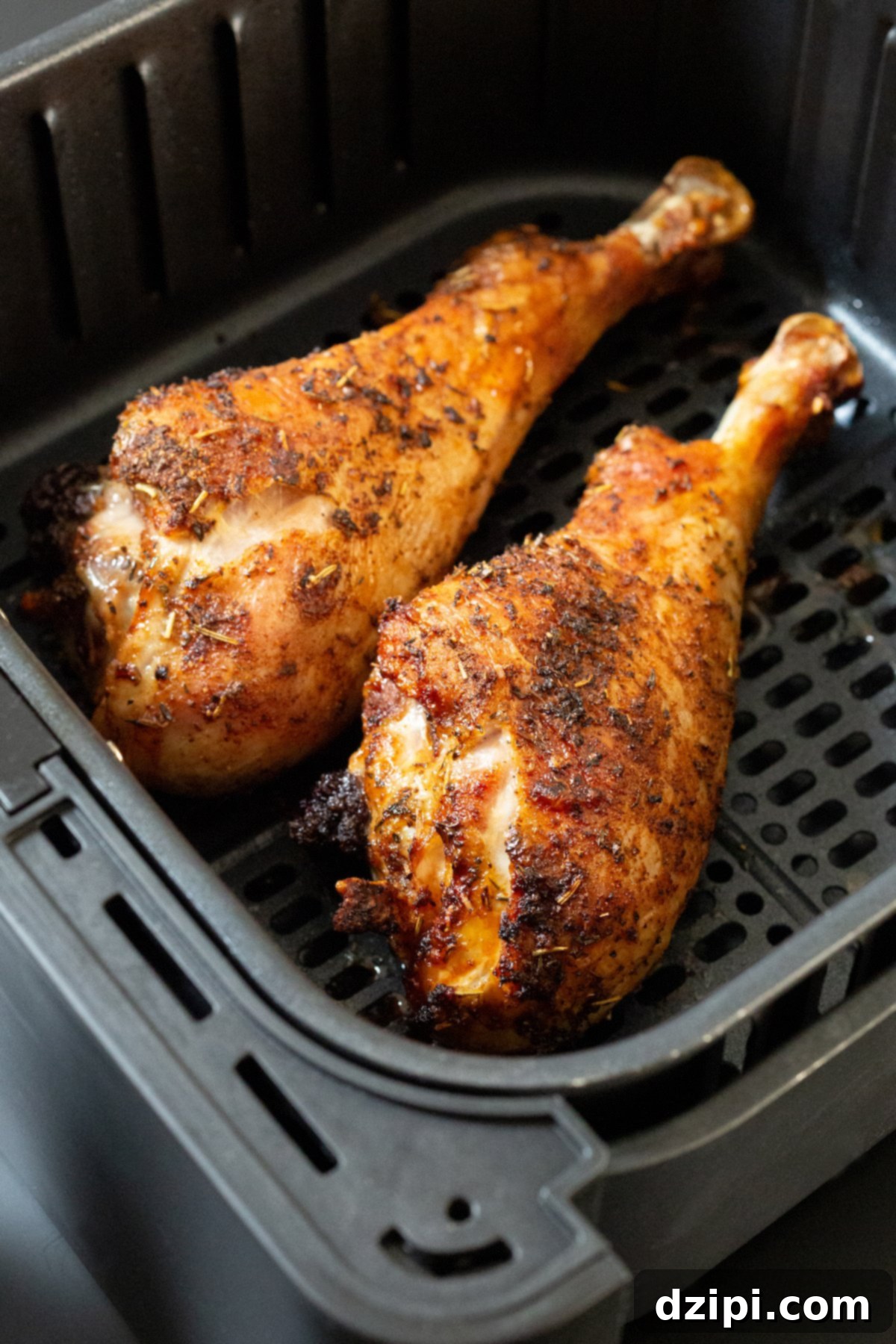 A black air fryer basket showcasing two beautifully cooked, golden-brown turkey legs, ready to be served.