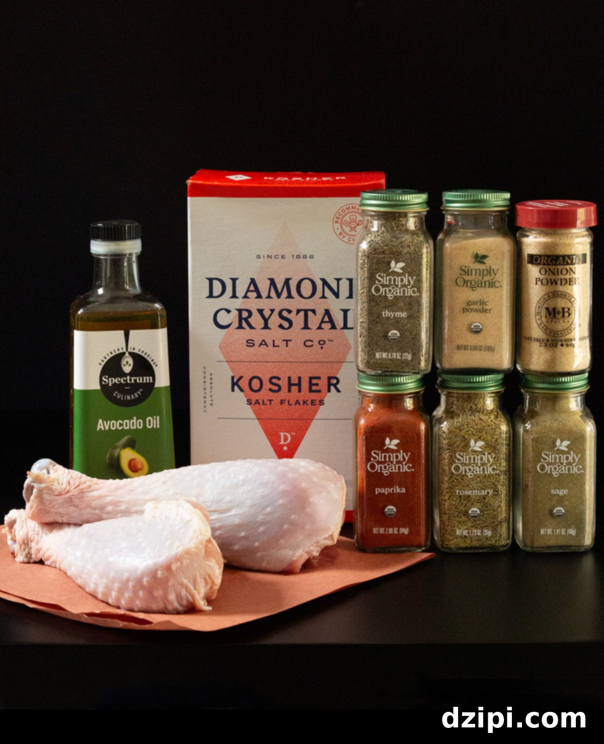 Two raw turkey legs, neatly arranged beside bottles of aromatic seasoning, a box of fine salt, and a bottle of healthy avocado oil, all set against a sleek black background.