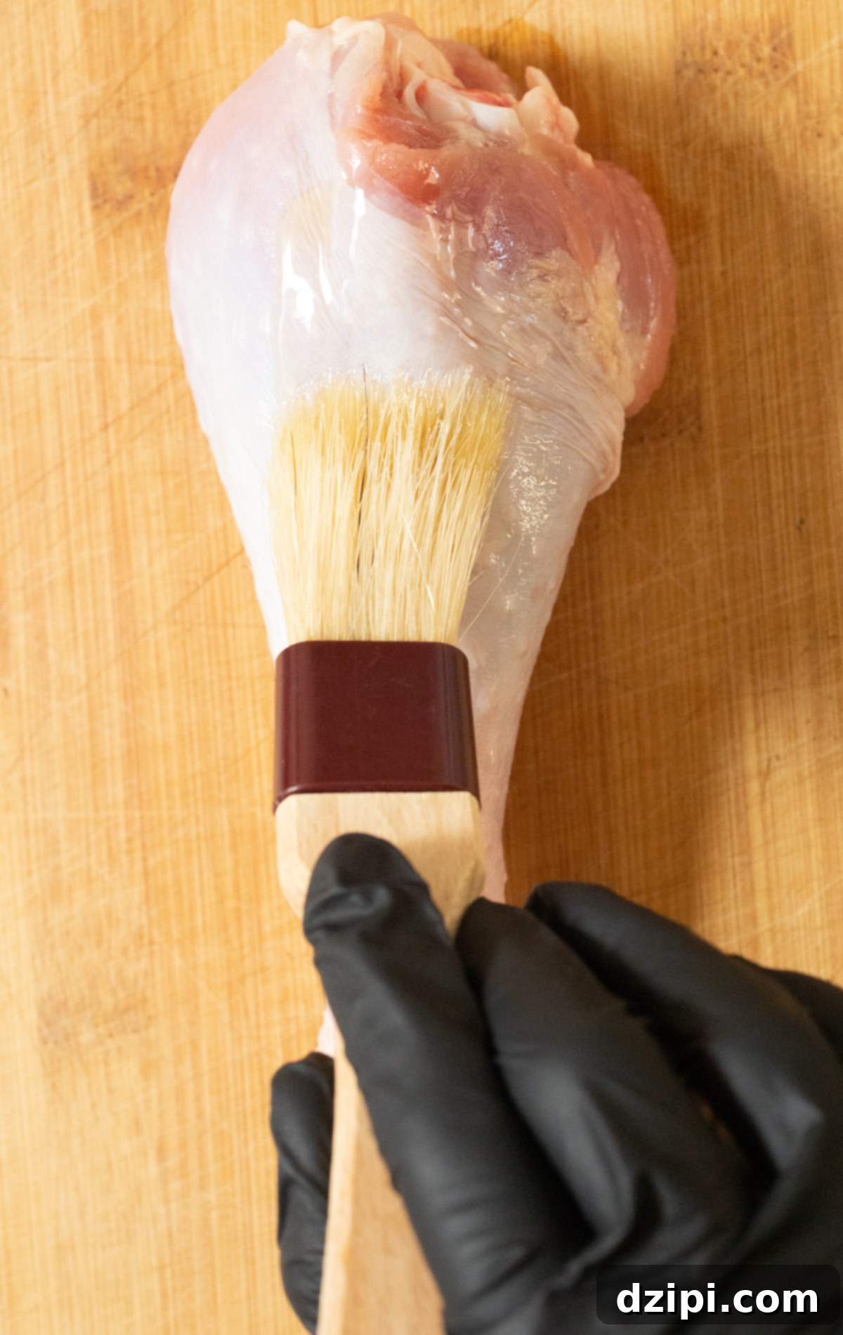 A raw turkey leg being meticulously brushed with oil using a pastry brush, ensuring even coating.