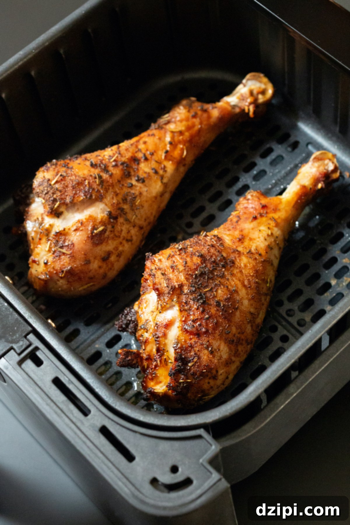 Two golden-brown, perfectly cooked turkey legs nestled in an air fryer basket, steam gently rising.