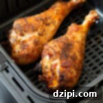 A black air fryer basket with two cooked turkey legs, golden and crispy.
