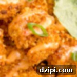 Close up of a single breaded fried shrimp that's drizzled in a orange colored bang bang sauce and garnished with a sliced green onion.