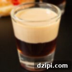 Jam Doughnut Poppers 6 A shot glass filled with a layer of raspberry liqueur and a top layer of Irish cream is in focus in the foreground. Another is out of focus in the background next to a jelly donut.