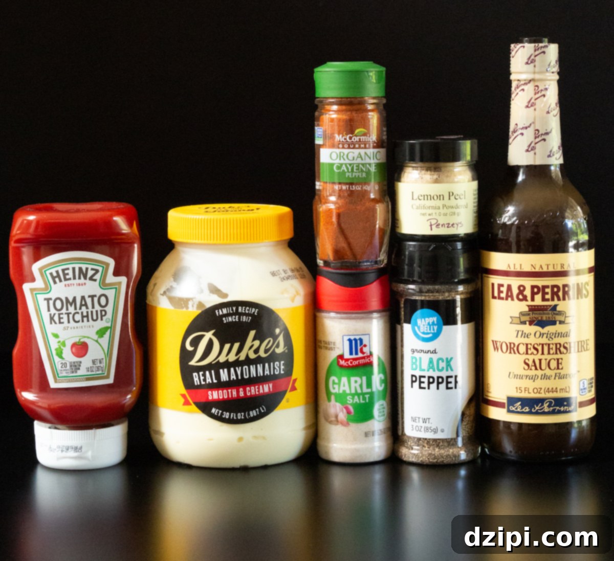 A bottle of ketchup, mayonnaise, garlic salt, cayenne pepper, black pepper, powdered lemon peel, and worcestershire sauce all on a black background.