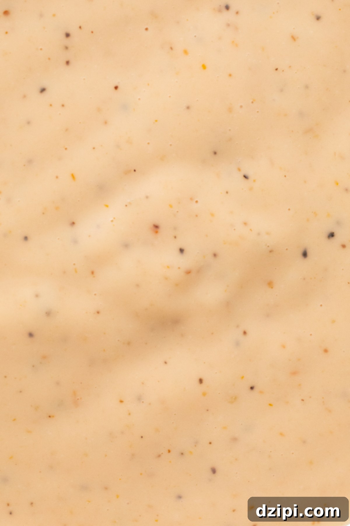 Extreme close up of a homemade Raising Cane's sauce where you can see large specs of black pepper and smaller specs of other seasonings.