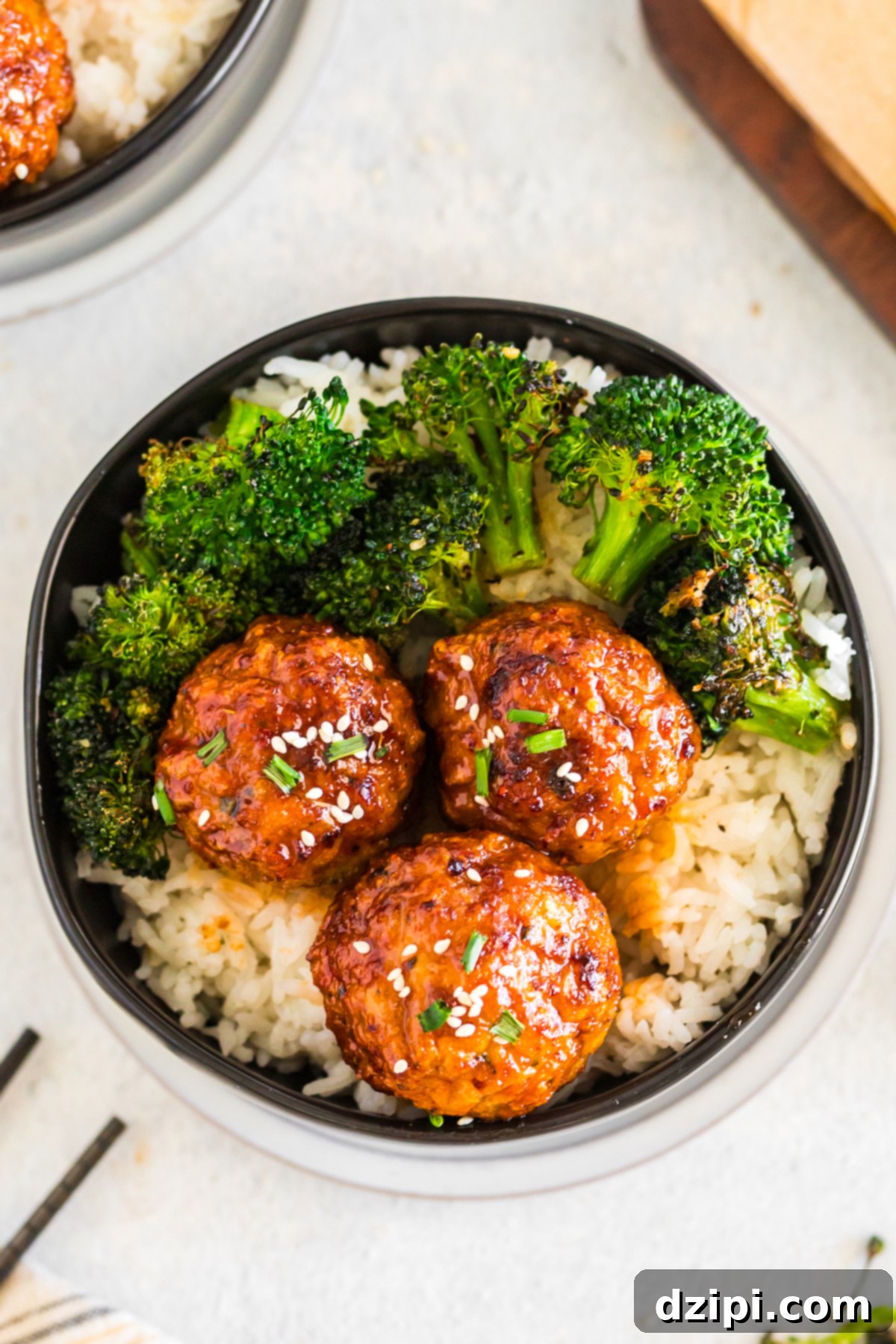 A bowl is filled with rice that's topped with three firecracker meatballs and steamed broccoli. 