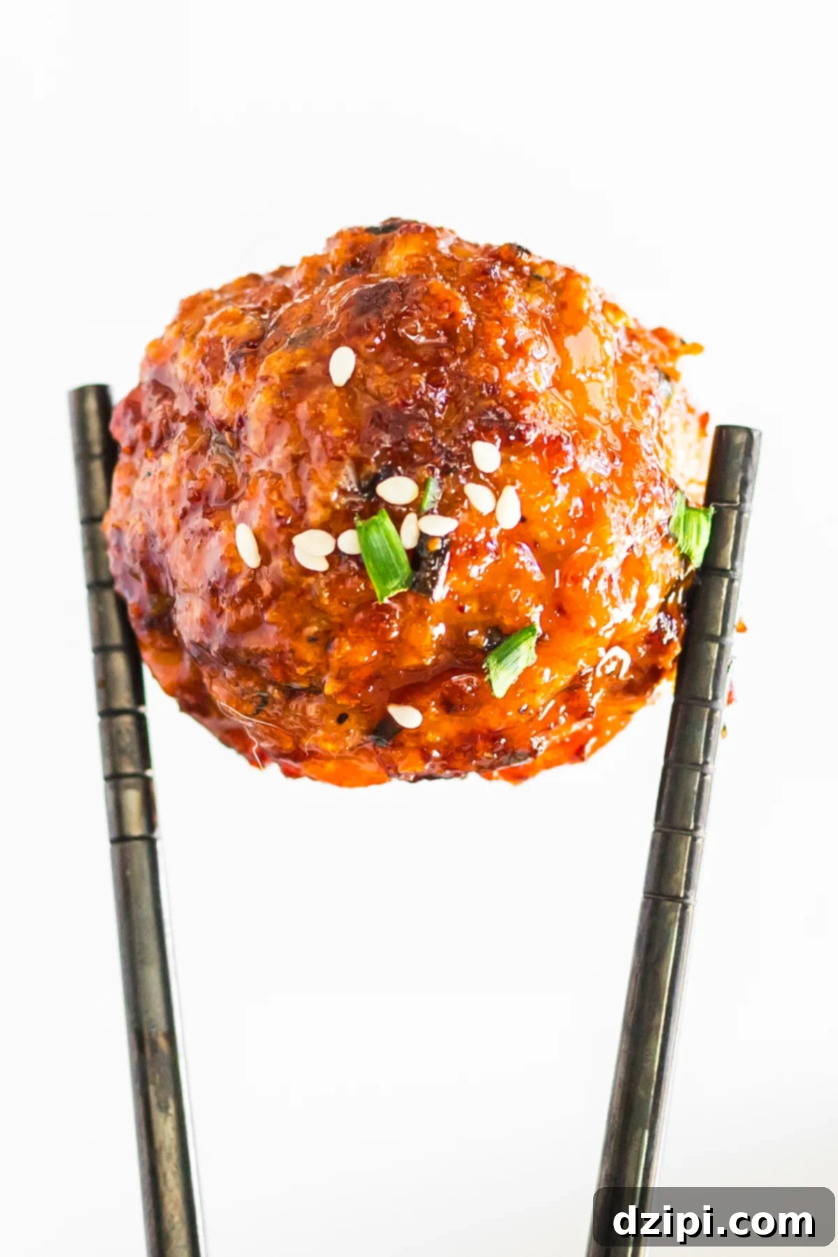 A pair of chopsticks holds up a single firecracker meatball against a white background.