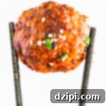 A pair of chopsticks holds up a single firecracker meatball against a white background.