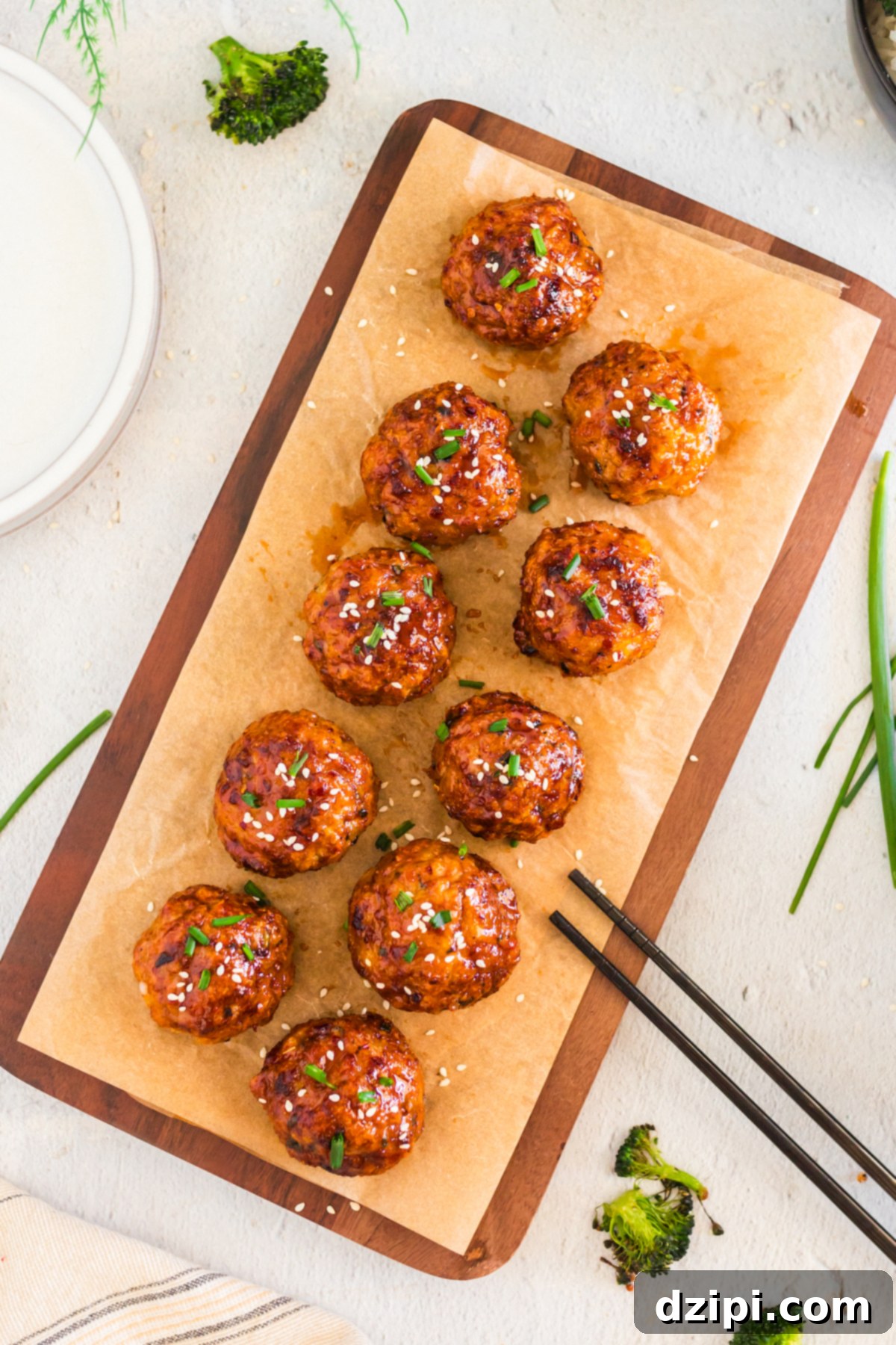 A long wooden board with 10 firecracker glazed meatballs next to a pair of chopsticks.