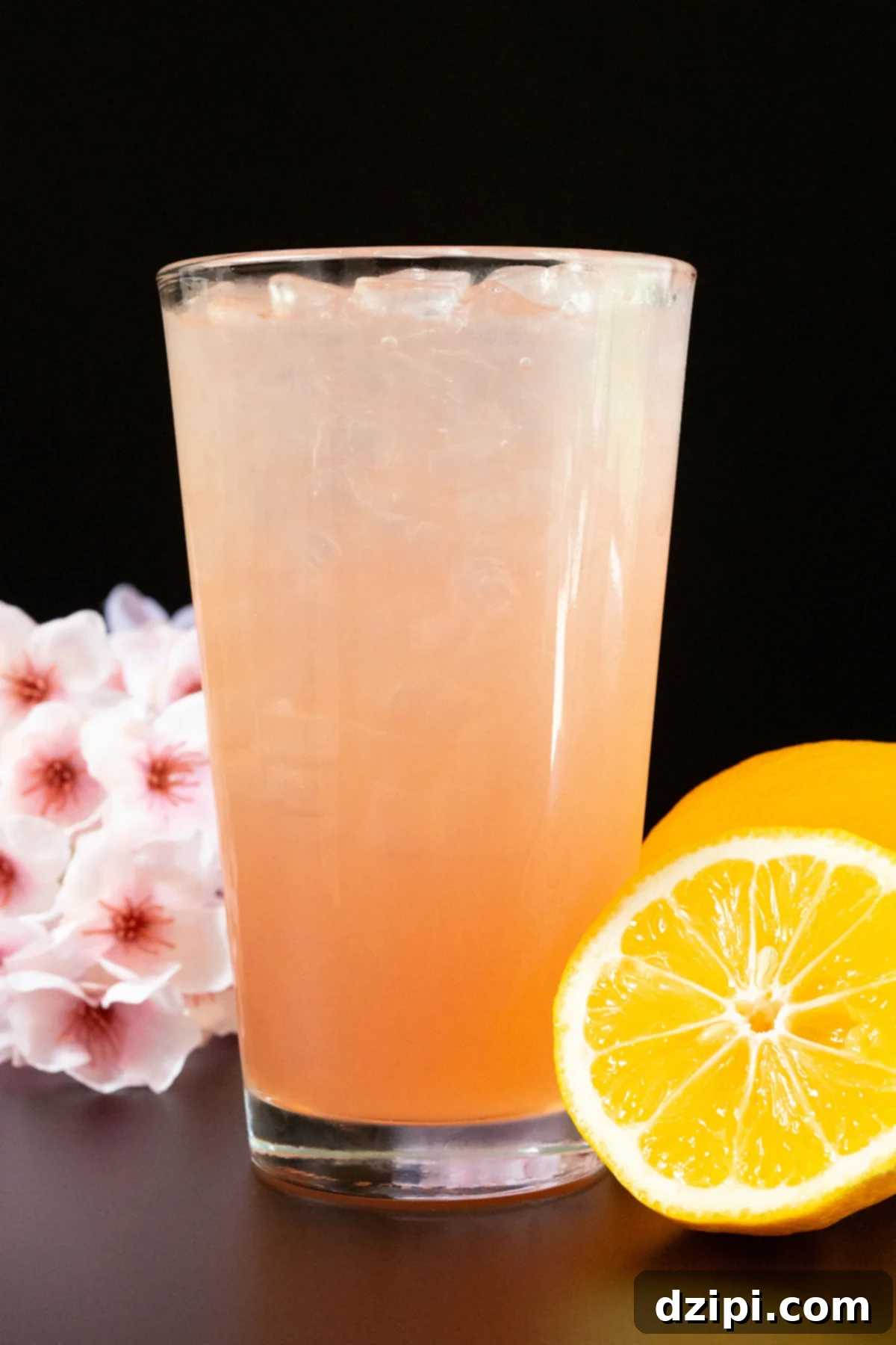 A pint glass filled with a light pink lemonade. Cherry blossoms and a sliced lemon are out of focus in the background.