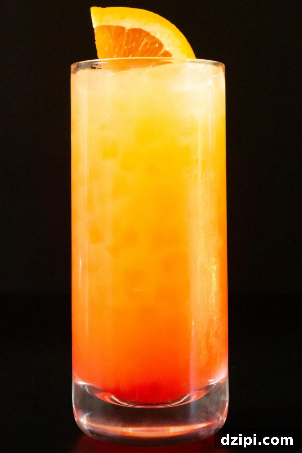 A tall highball glass filled with a vibrant Vodka Sunrise cocktail, showcasing a beautiful gradient from yellow-orange to deep red, garnished with a fresh orange slice, sitting on a sunlit surface.