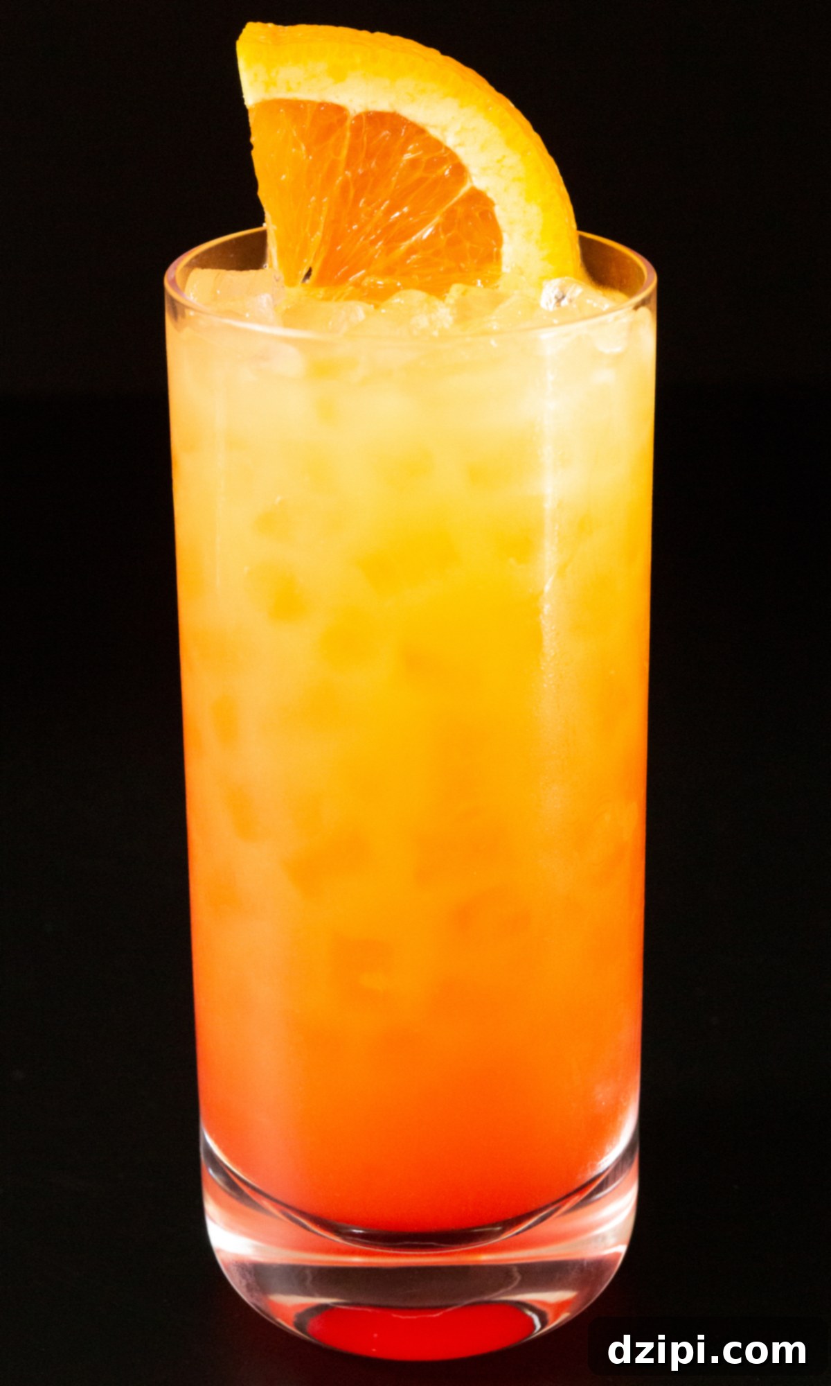 A highball glass filled with an appealing Vodka Sunrise cocktail, showcasing a perfect gradient of yellow, orange, and red, adorned with an orange slice and maraschino cherry, set against a blurred bright background.