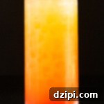 A highball glass is filled with orange juice and grenadine that makes it look like a sunrise. A sliced orange is used as garnish.