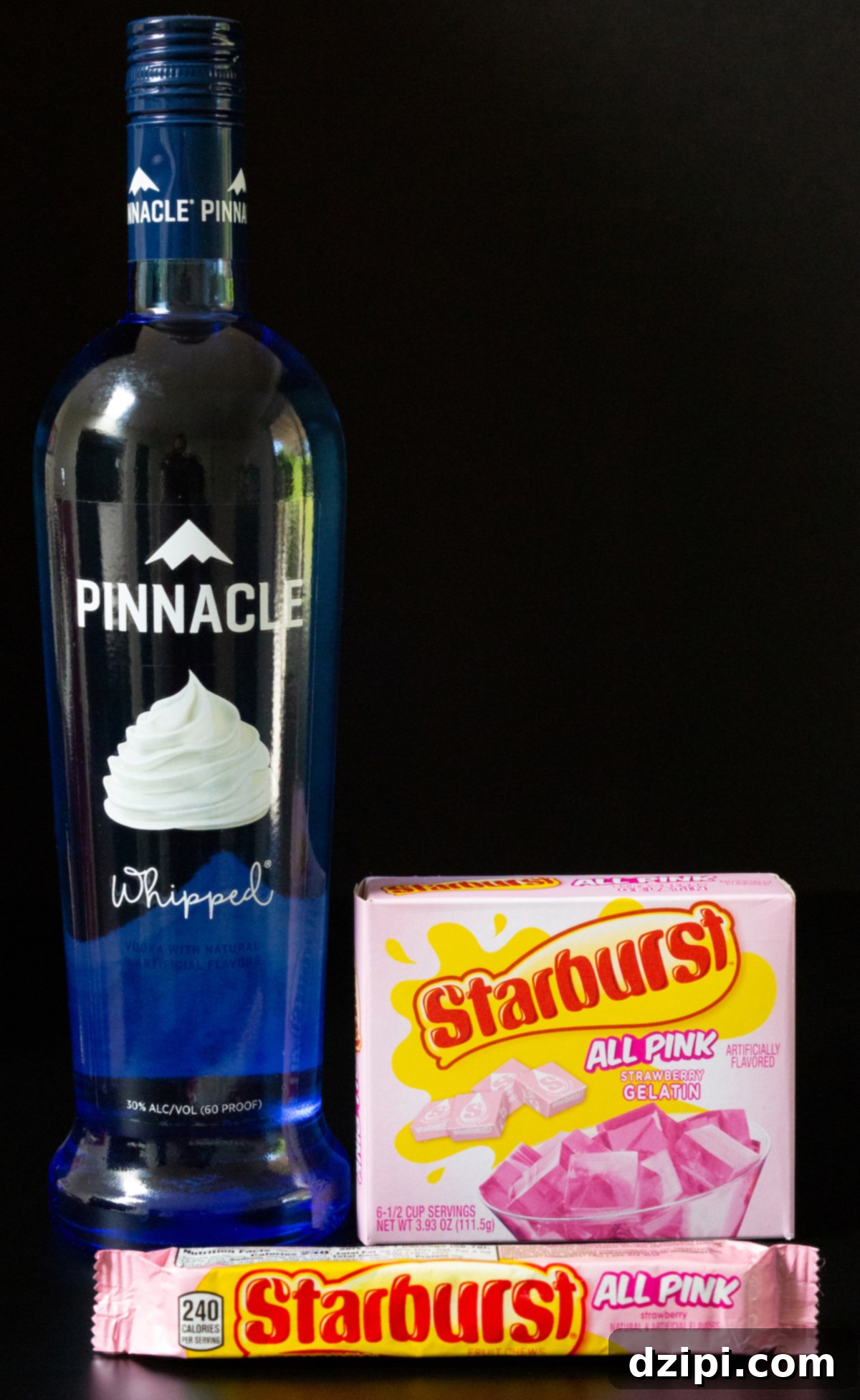 A bottle of whipped cream flavored vodka, a box of pink Starburst gelatin, and a package of all pink Starburst candy, all set against a dark background.
