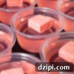 Ten pink jello shots topped with unwrapped Starburst candies on a black background, showcasing the vibrant treats.