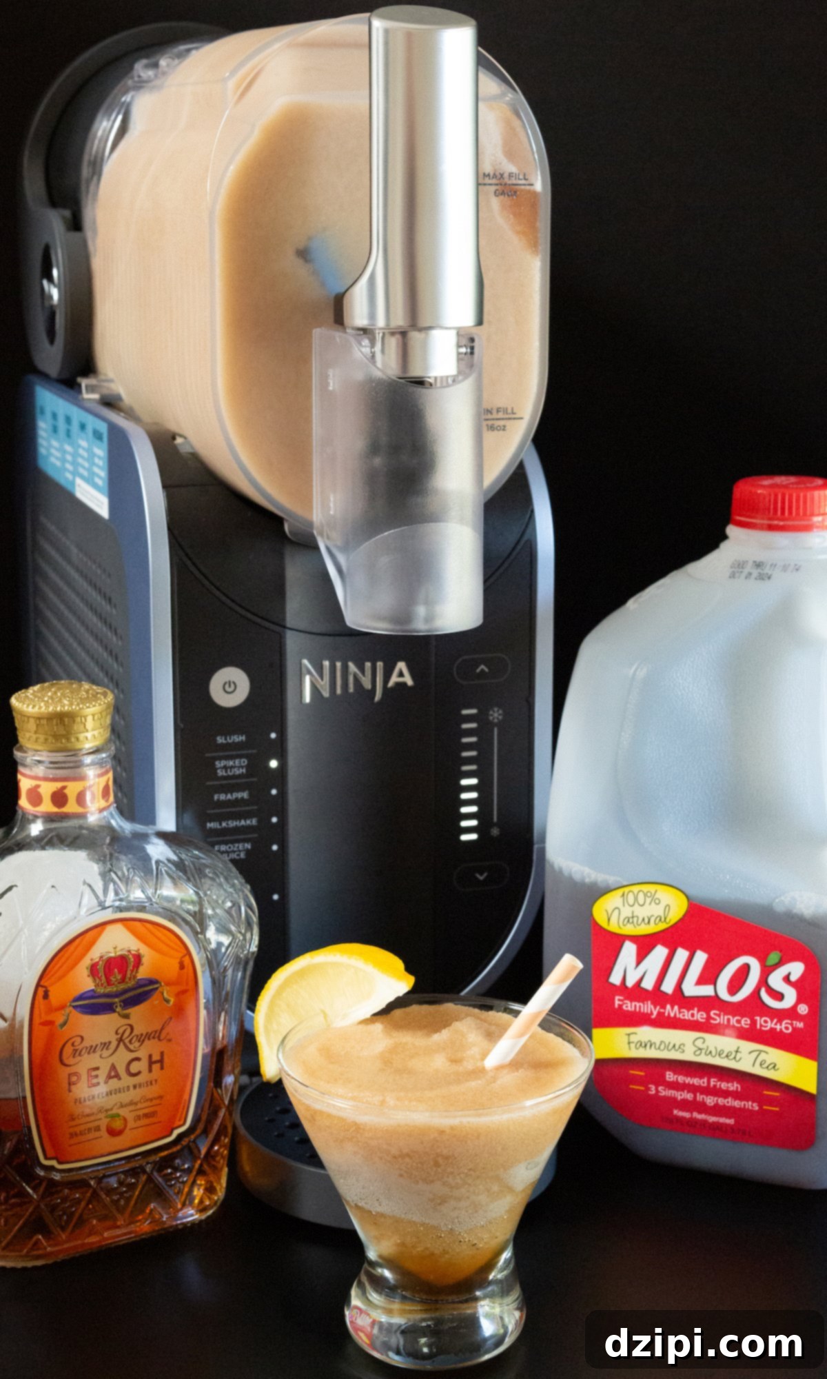 A Ninja Slushi appliance filled with a light brown colored slushy, in front of a prepared stemless martini glass filled with a slushy. A bottle of Crown Royal peach and gallon of sweet tea on the sides.