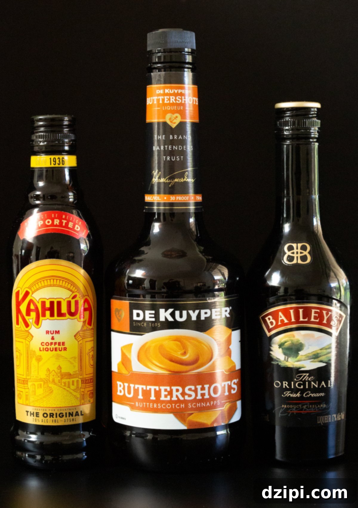 Golden Peanut Crunch Shot 3 A high-quality image of bottles of Kahlua, Butterscotch Schnapps, and Bailey's Irish Cream arranged on a sleek black background, highlighting the key ingredients for the Butterfinger Shot.