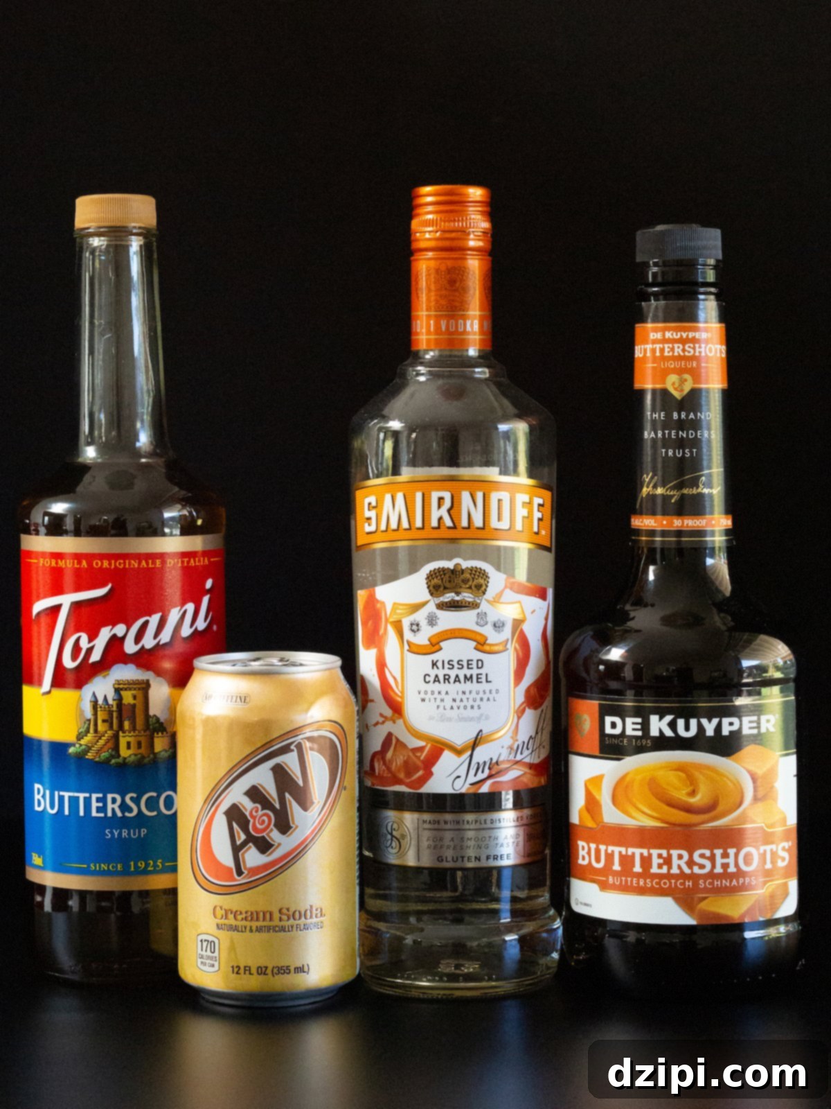 A group of bottles and a can on a black background: Butterscotch syrup, a can of A&W cream soda, Smirnoff Kissed Caramel vodka, and Buttershots Butterscotch schnapps.