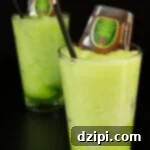 Crown's Crisp Green Apple Slush 4 Two pint glasses filled with a vibrant, neon green Crown Apple Slushie, each topped with a mini bottle of Crown Royal Apple whiskey and a black straw.