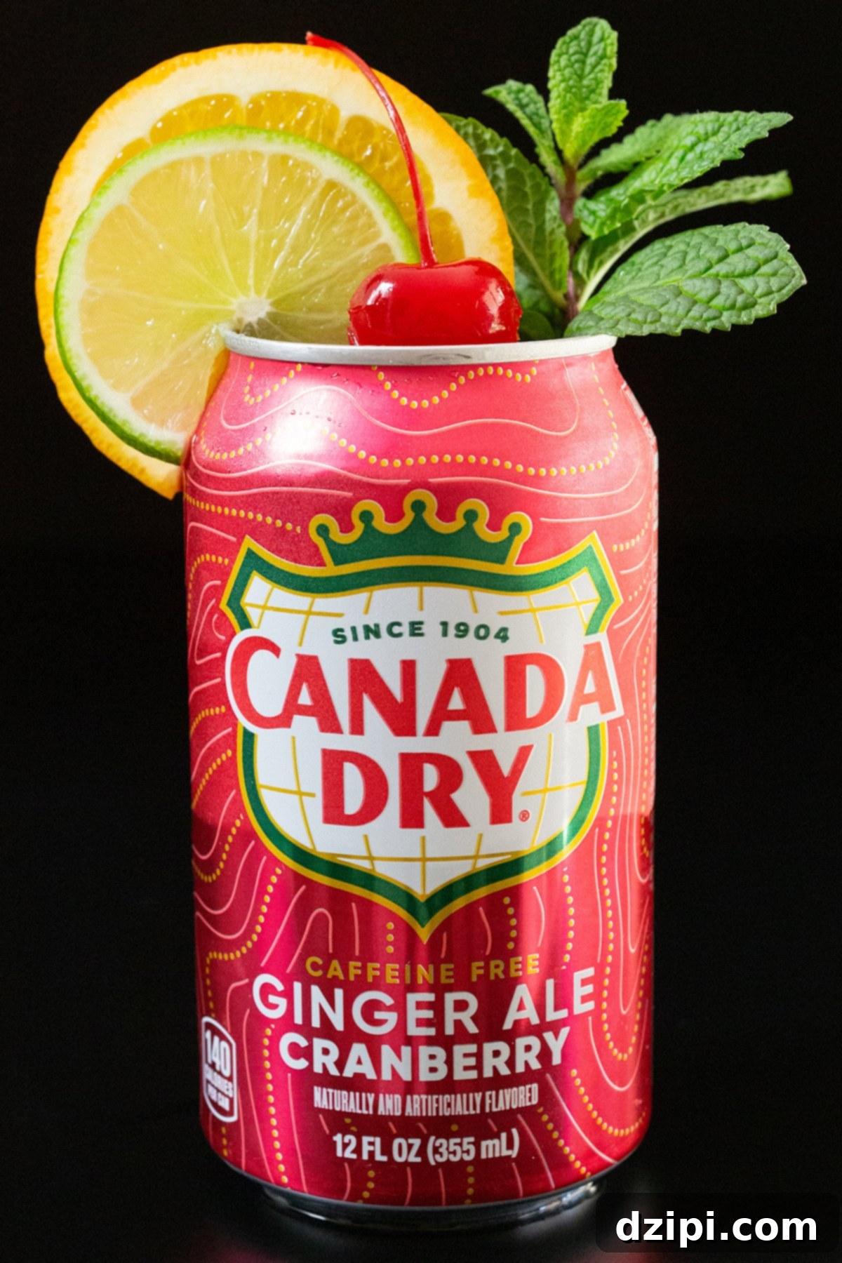 A can of cranberry flavored ginger ale has had the top removed and is garnished with a lime wheel, an orange wheel, a sprig of mint, and a maraschino cherry in the middle.