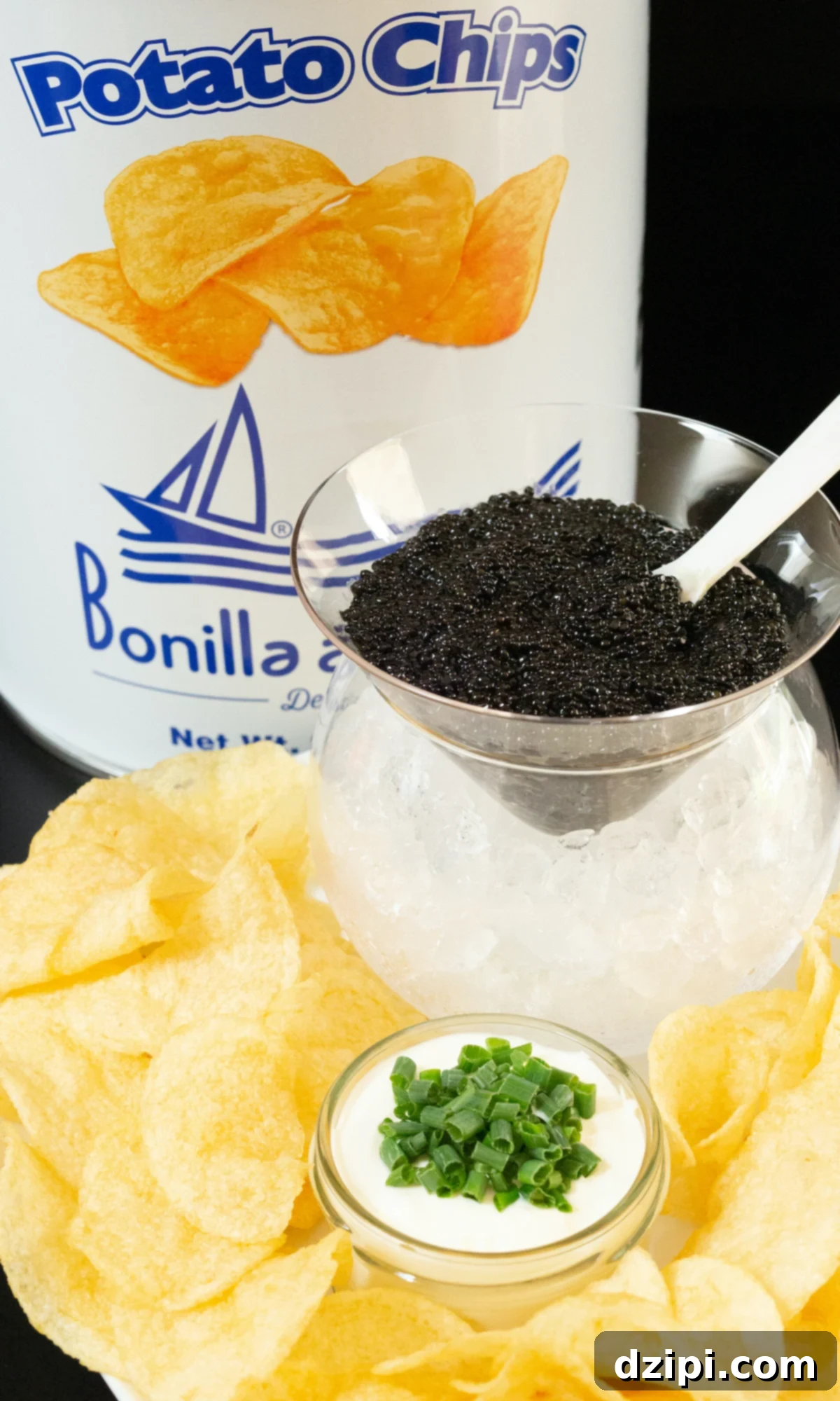 A tin of potato chips, a glass caviar chiller with ice on the bottom and caviar on top, and a plate of potato chips with a jar of creme fraiche topped with sliced green onions.