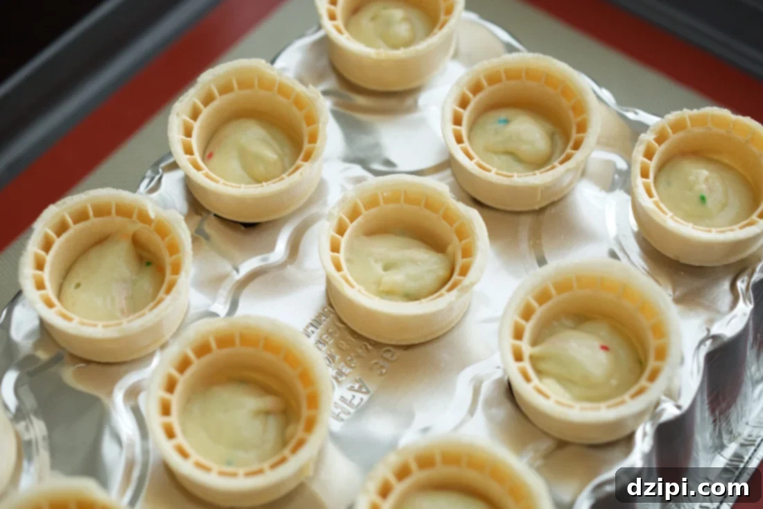Ice cream cones filled with cupcake batter before going in the oven, neatly arranged in a custom aluminum pan.