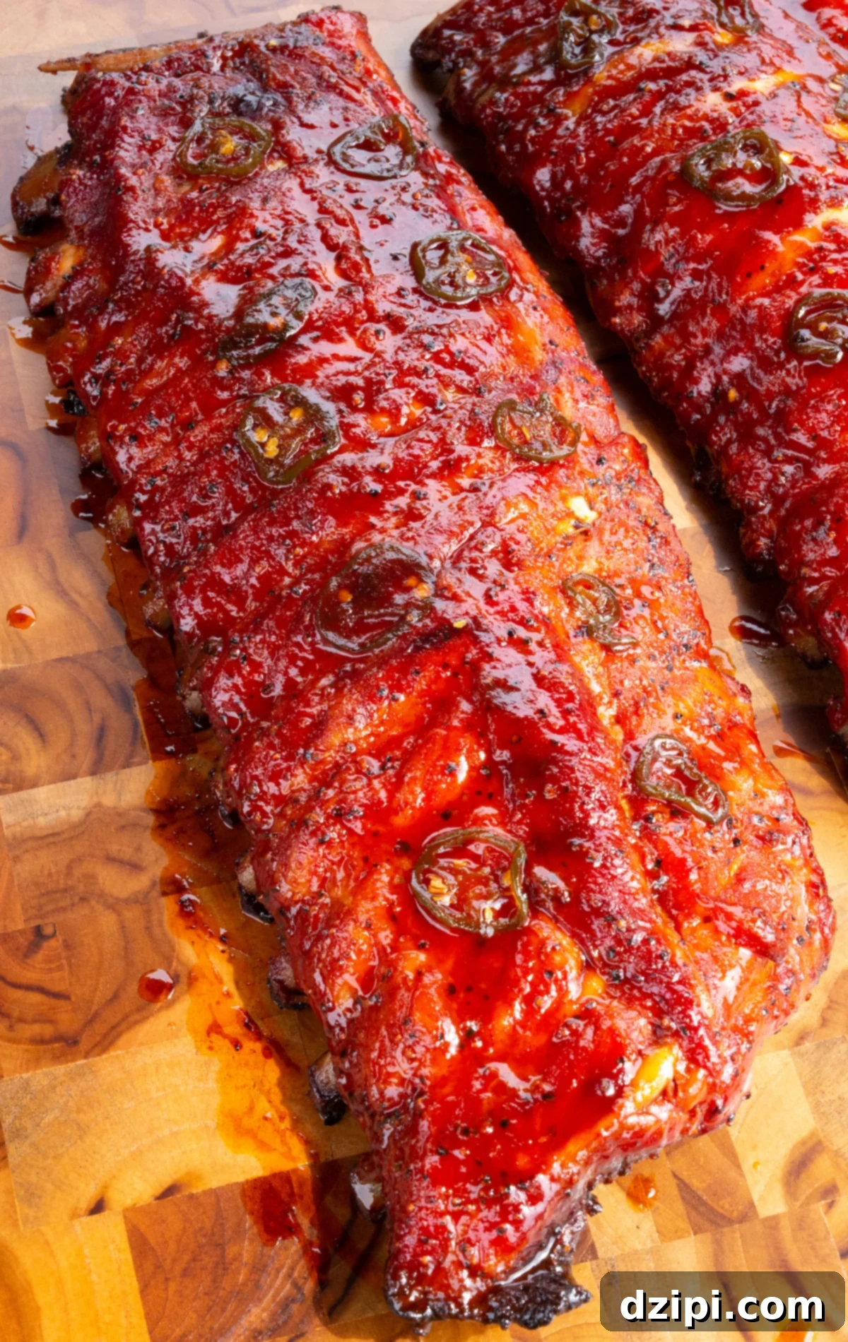 A cooked rack of ribs covered in a bright red candy coating and topped with sliced jalapeños on a cutting board, ready to be served.
