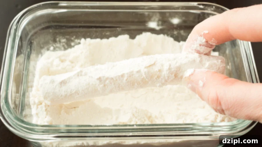 A mozzarella cheese stick being rolled in a bowl of flour as the first step of coating