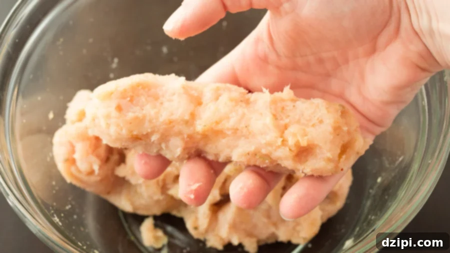 A mozzarella stick, coated in flour and egg, is now being carefully wrapped in seasoned ground chicken