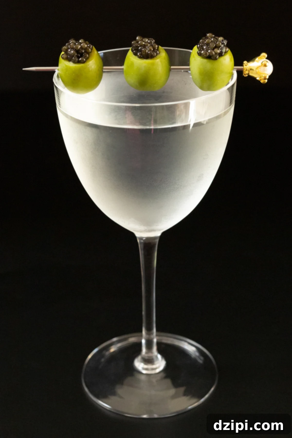 A frosted Nick & Nora glass filled with a martini that's garnished with a cocktail pick with three skewered green olives stuffed with caviar.