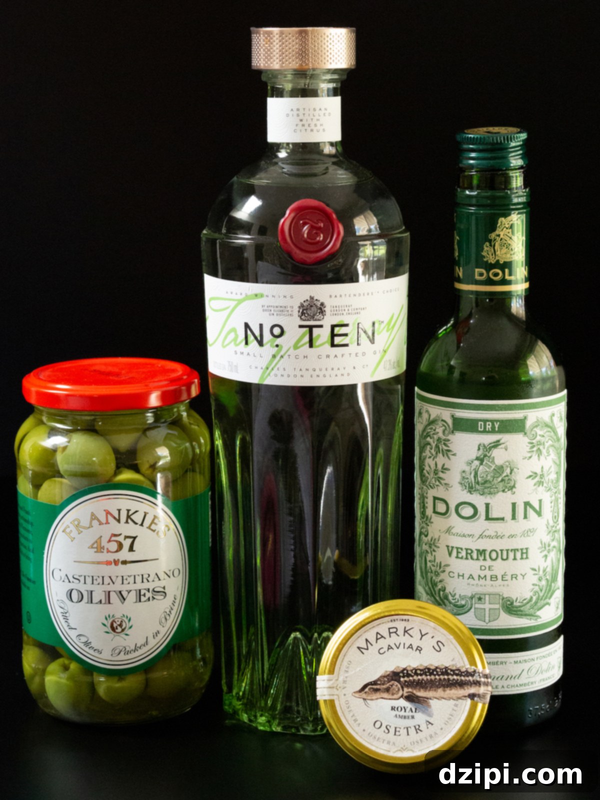 A jar of Castelvetrano olives, a bottle of No. Ten gin, a bottle of Dolin dry vermouth, and a tin of Royal Amber Osetra caviar on a black background.