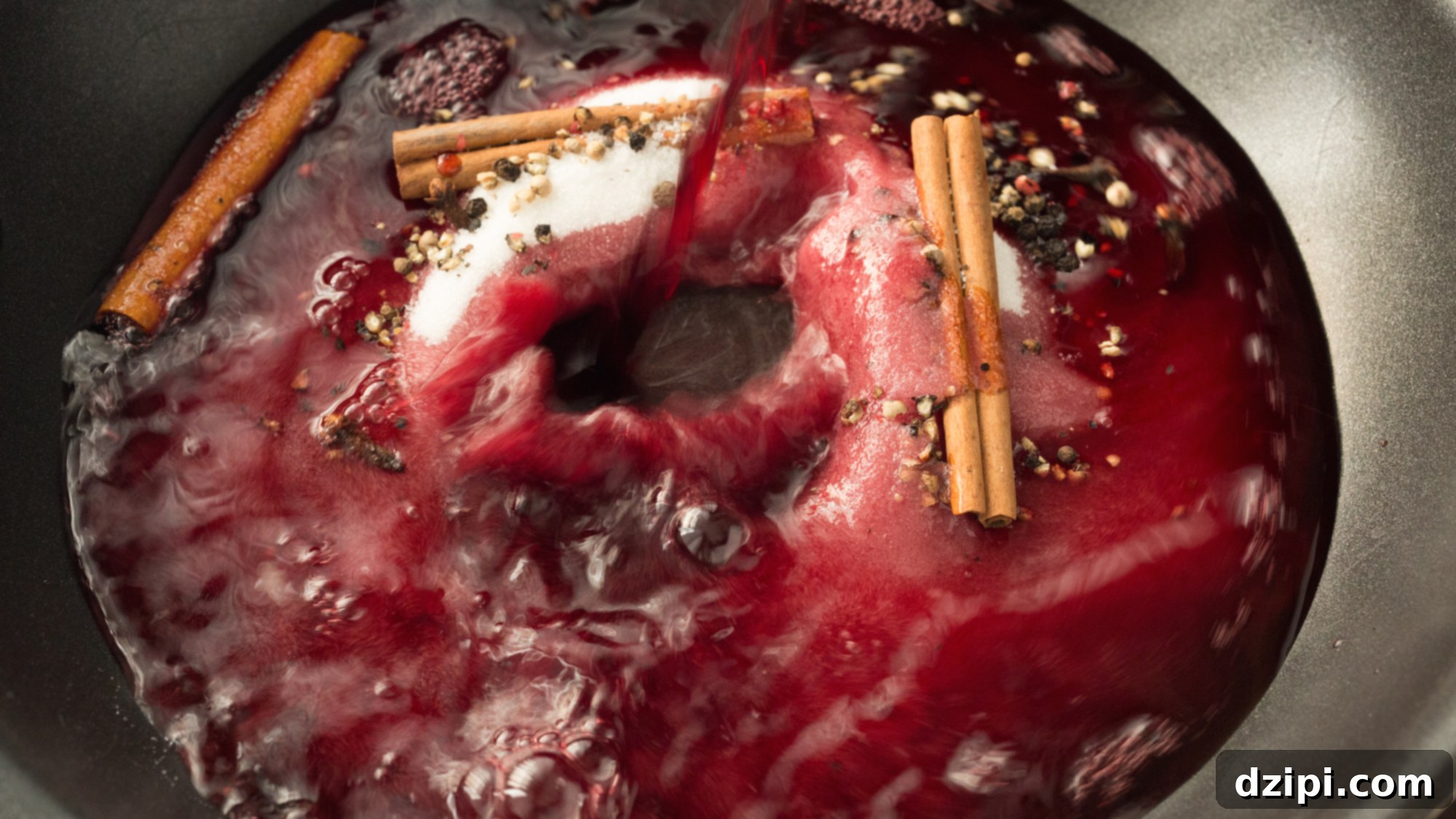 Red wine being poured into a skillet with sugar, cinnamon sticks, and various spices, showcasing the preparation of the aromatic Spiced Red Wine Syrup.