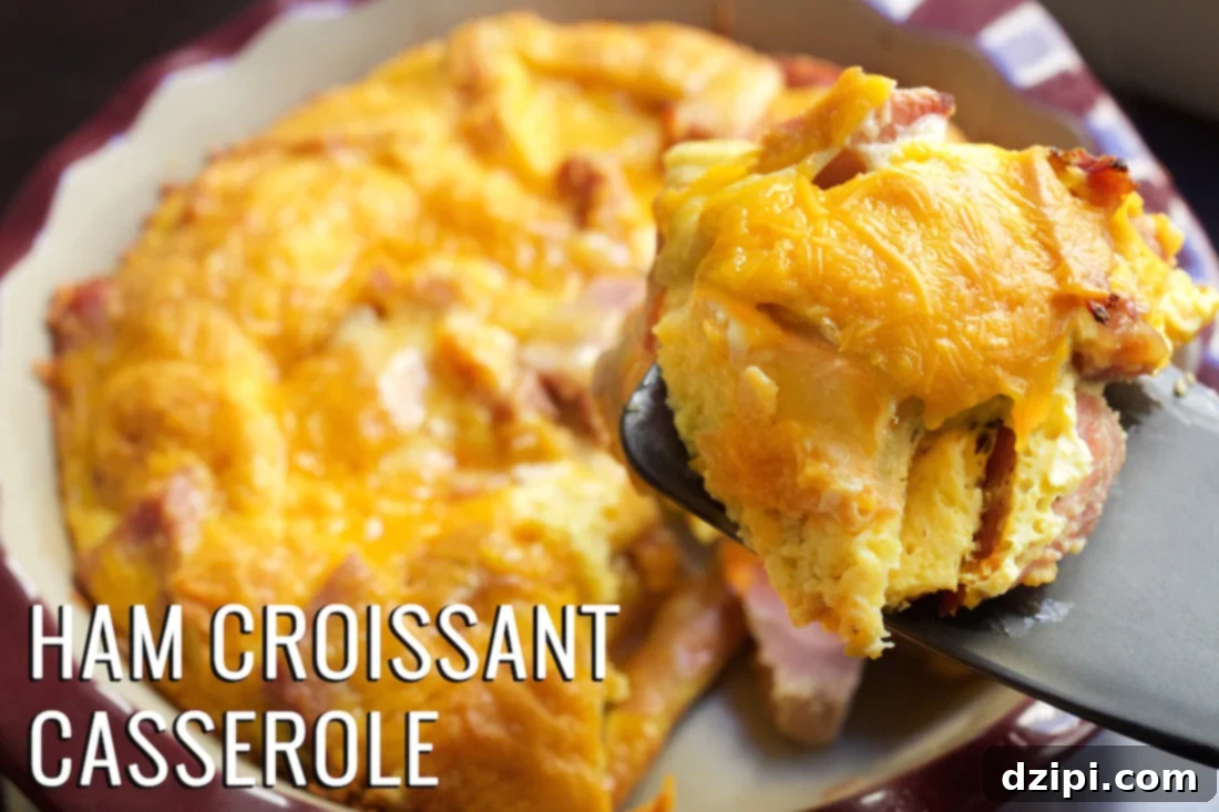 A spatula holds up a piece of ham and croissant breakfast casserole with the casserole dish in the background
