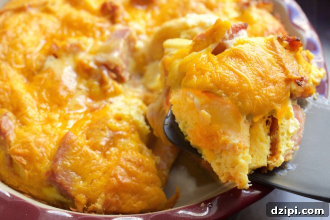 A spatula holds up a piece of ham and croissant breakfast casserole with the casserole dish in the background