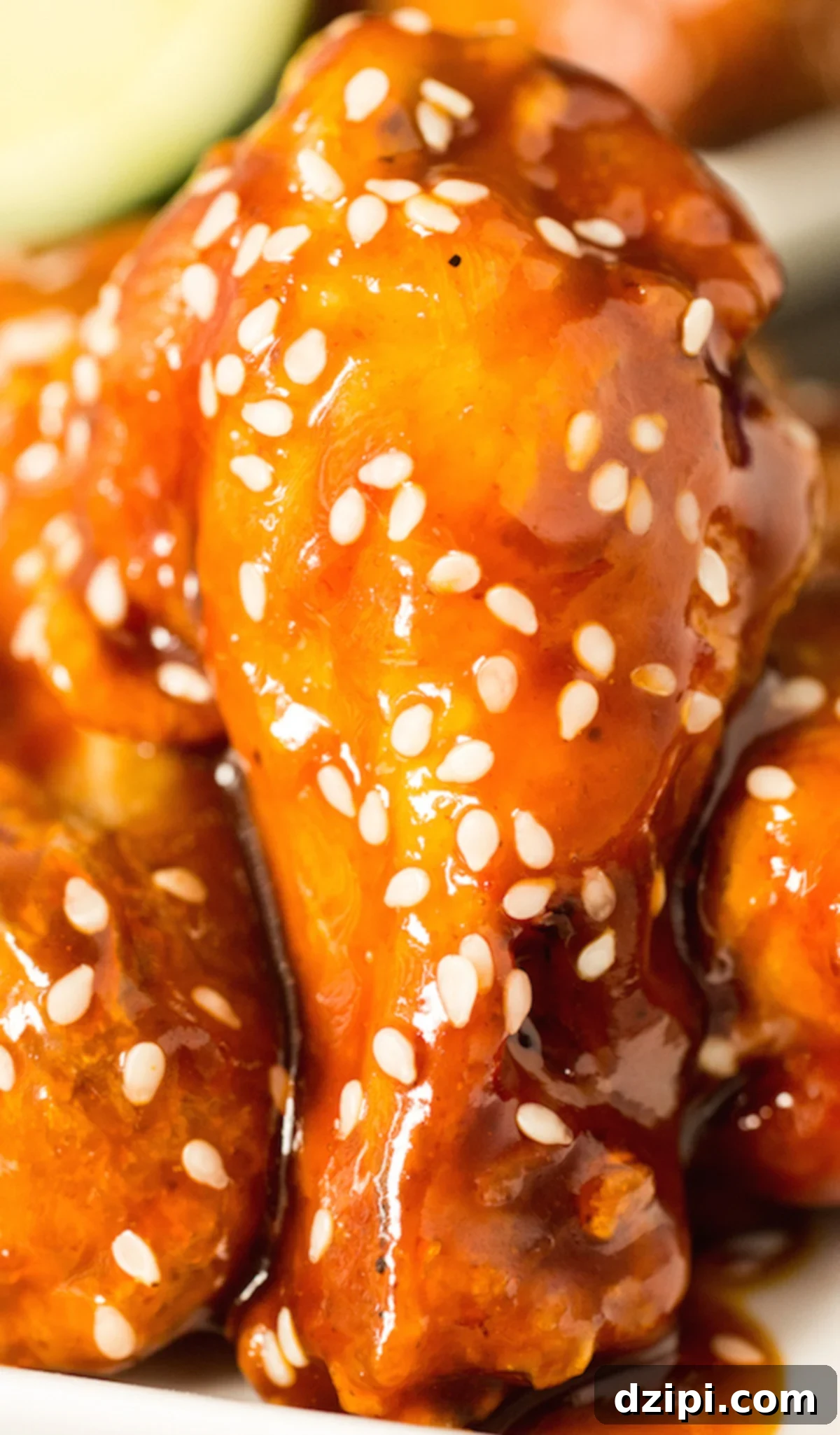 Sticky Honey Sriracha Wings 4 An extreme close up of a drumette wing covered in the orange sriracha honey lime sauce and white sesame seeds as garnish.