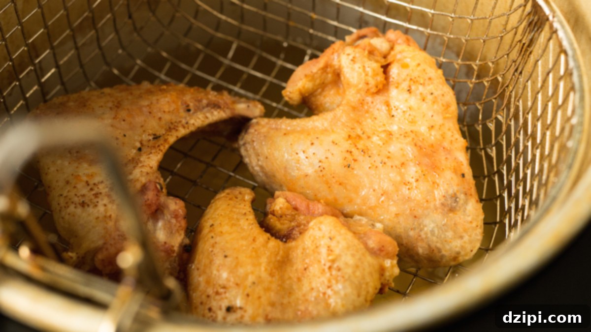 Sticky Honey Sriracha Wings 5 Crispy, golden brown wings in a deep fryer basket.