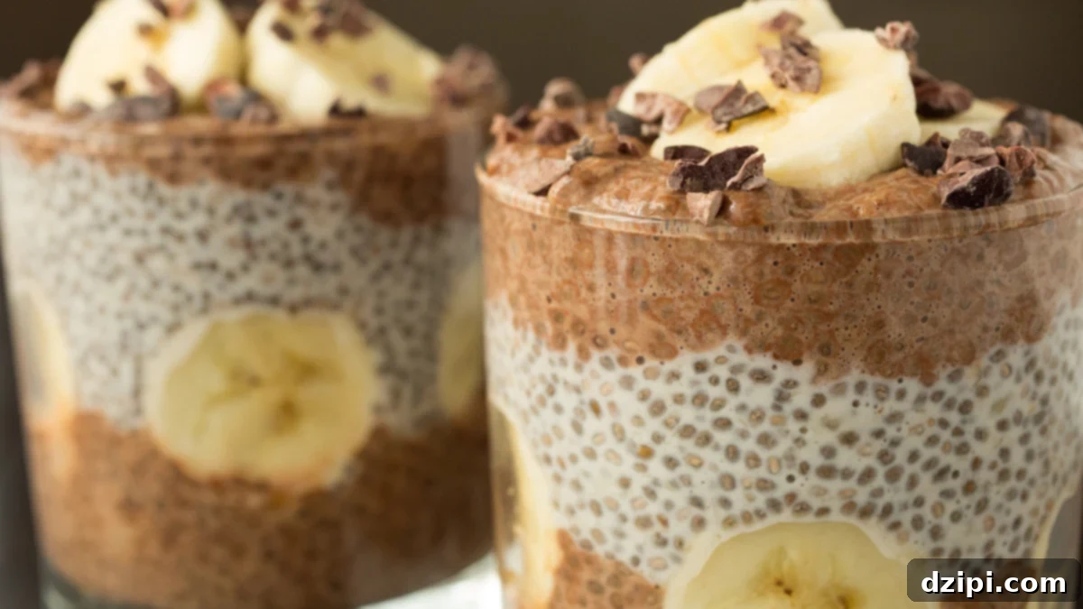 Two exquisite lowball glasses are meticulously filled with layers of creamy banana chocolate chia pudding, elegantly crowned with fresh banana slices and crunchy cacao nibs. This vibrant breakfast offers a delightful blend of taste and nutrition.